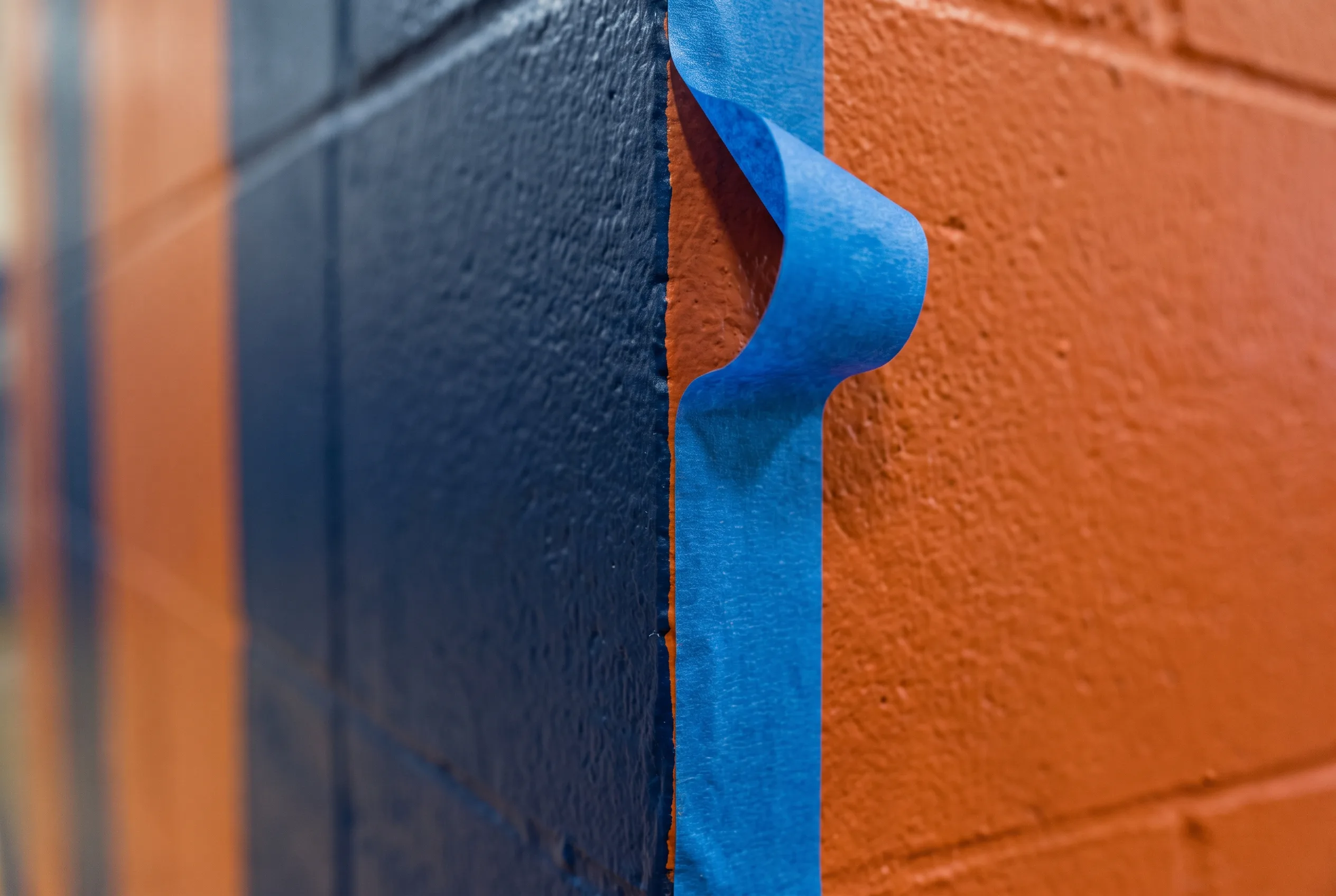 Close-up of painter's tape being pulled from a freshly painted block wall