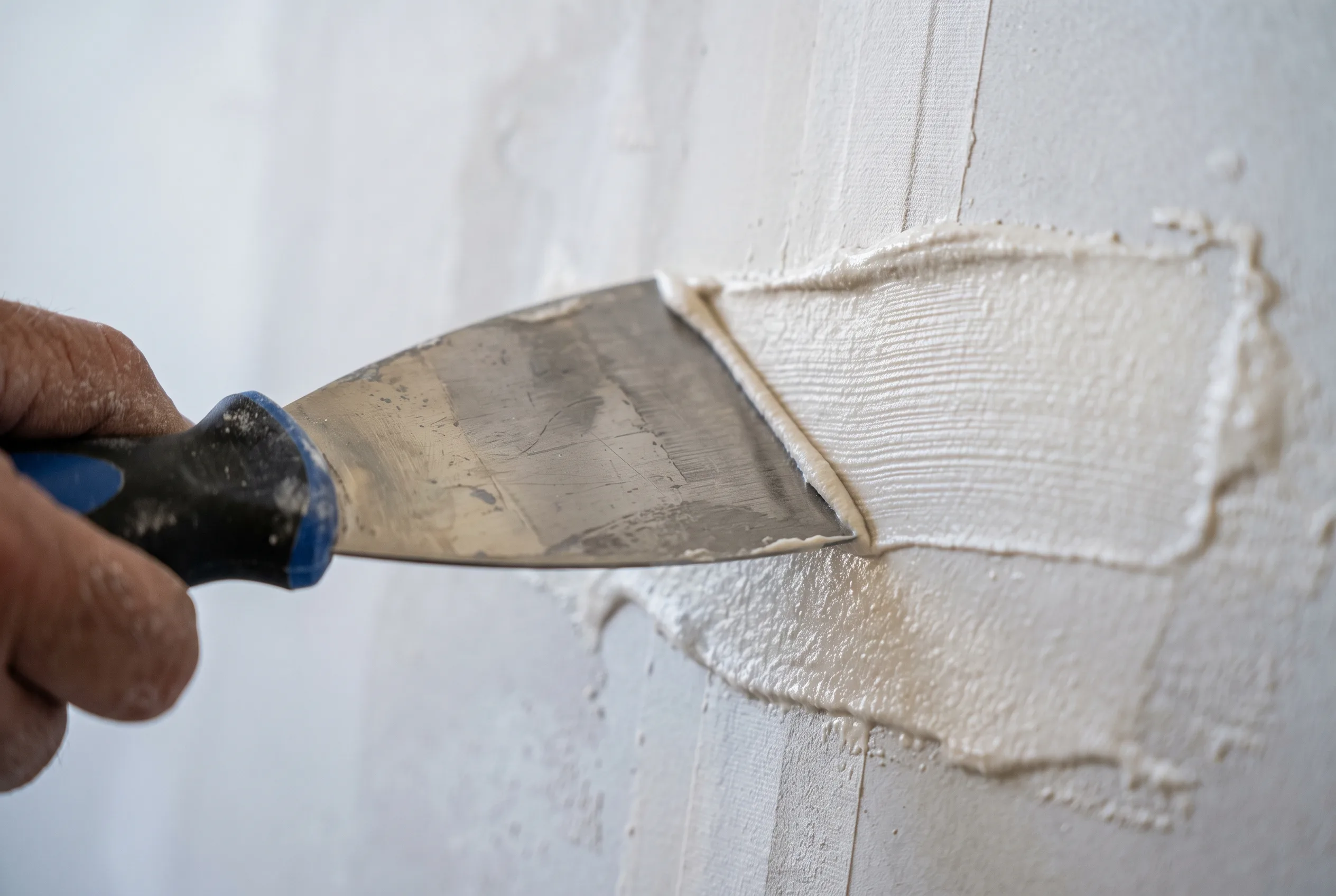 Close-up of a skim coating knife smoothing a wall